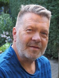 Een man in een blauw shirt tegen een natuurachtergrond