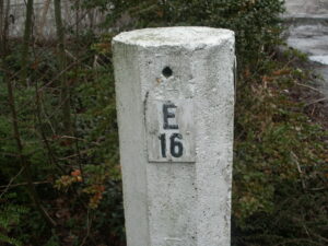 Wit bordje met E16 op een witte betonnen paal